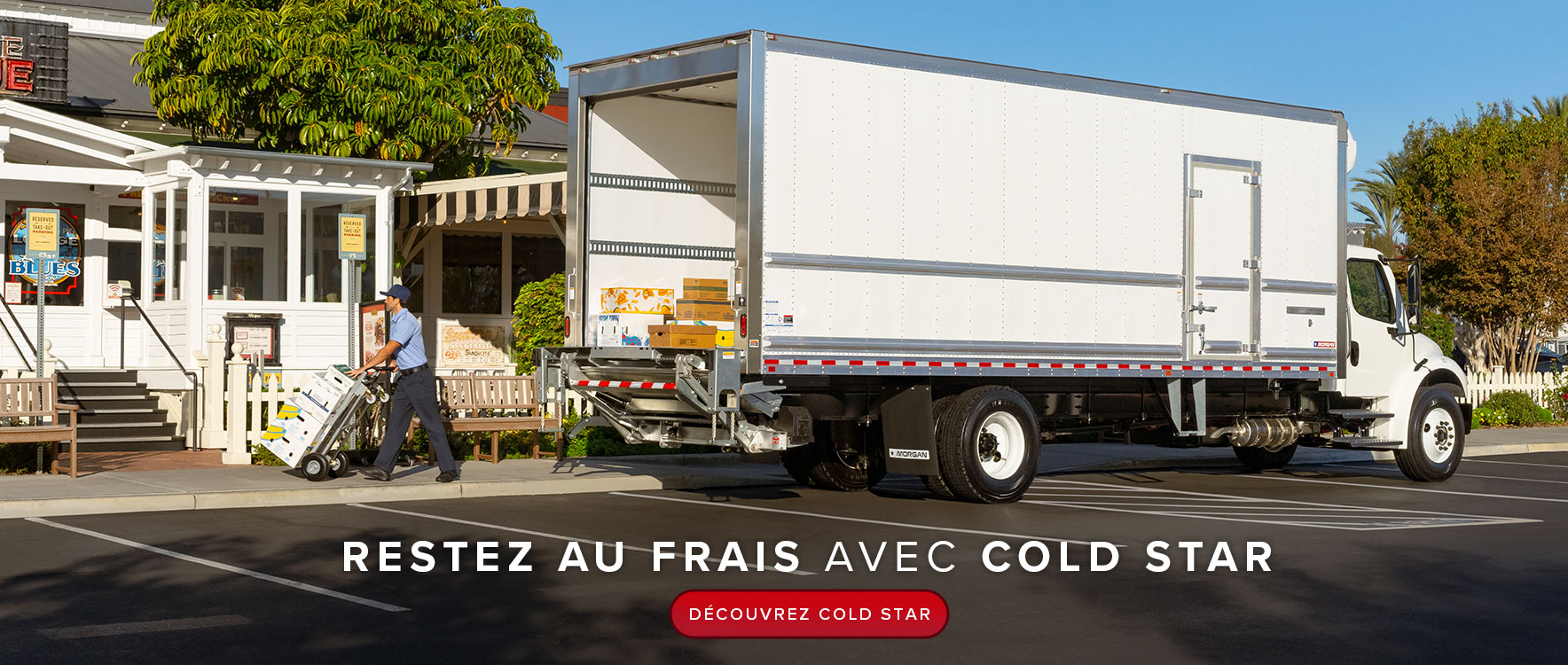Un grand camion frigorifique blanc est garé devant un restaurant BBQ. Un livreur transporte des boîtes de produits frais sur un diable en se dirigeant vers la porte d'entrée.