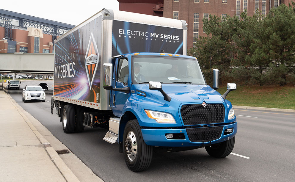 Grande benne sèche avec autocollants entiers, montée sur un châssis bleu de la série International MV, photographiée de face sur l’autoroute.