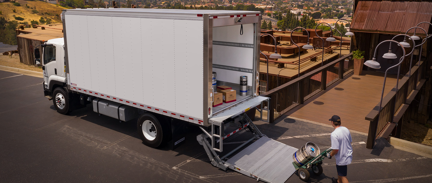 A person unloading beer kegs from a Refrigerated Cold Star truck body using a liftgate